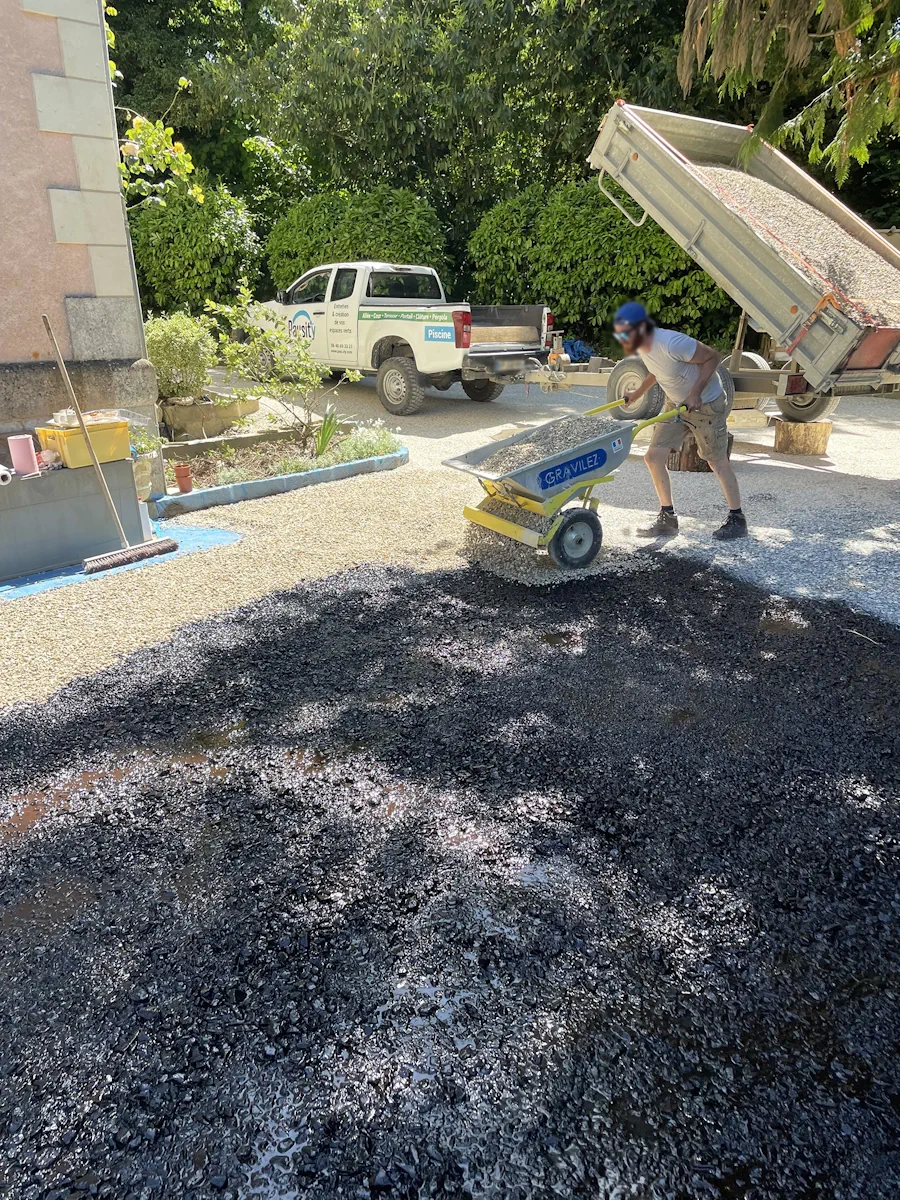 Compagnon déversant du gravier au moyen d'une brouette doseuse sur une surface encollée