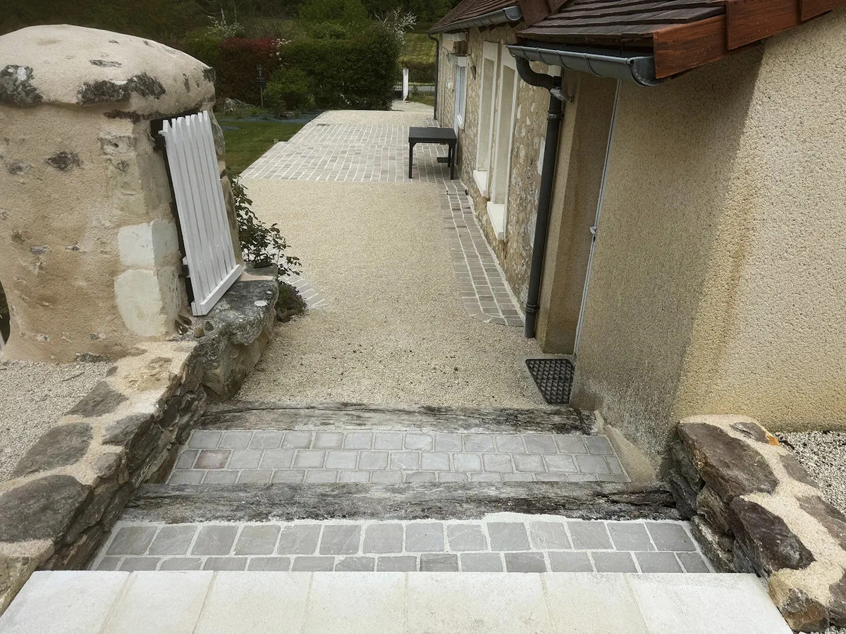 Cour en gravier clair et cheminement pavé longeant la façade en pierre