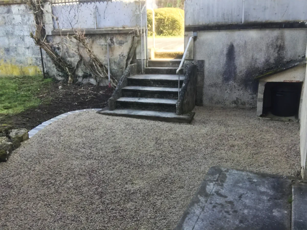 Cour en gravier stabilisé au pied d'un escalier de pierre, bordure claire en arc de cercle