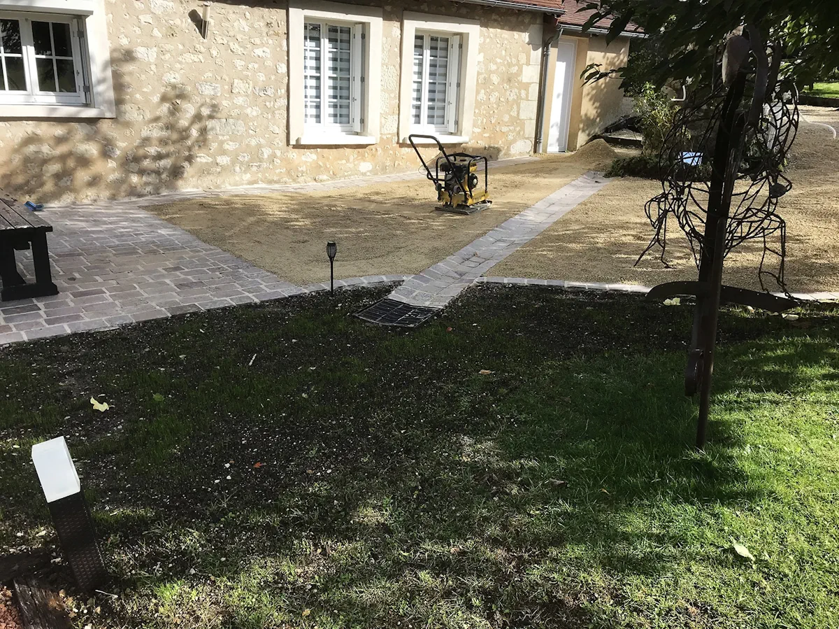 Cour terminée mêlant pavage, gravier et pelouse, devant une maison en pierre