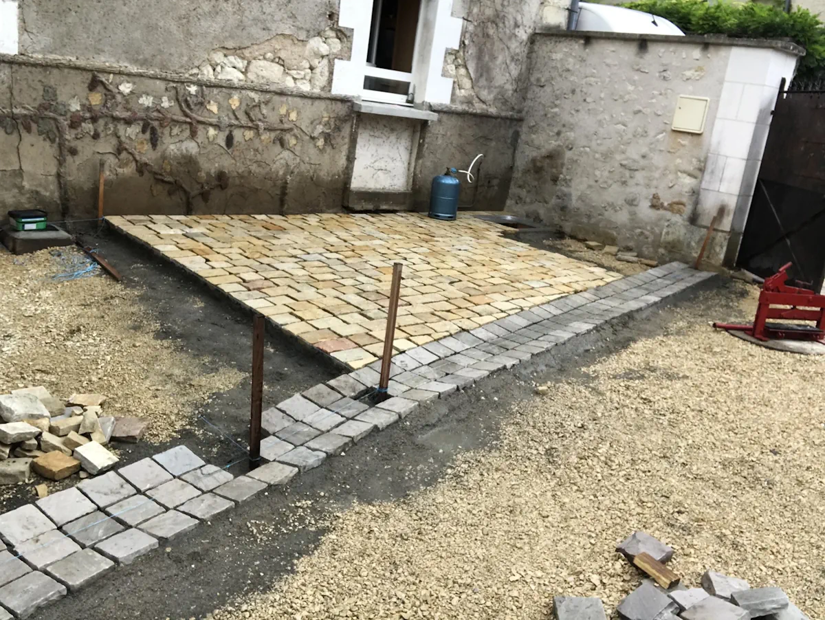 Terrasse en pavés de pierre dorée en cours de pose, entourée d'une bordure de pavés gris