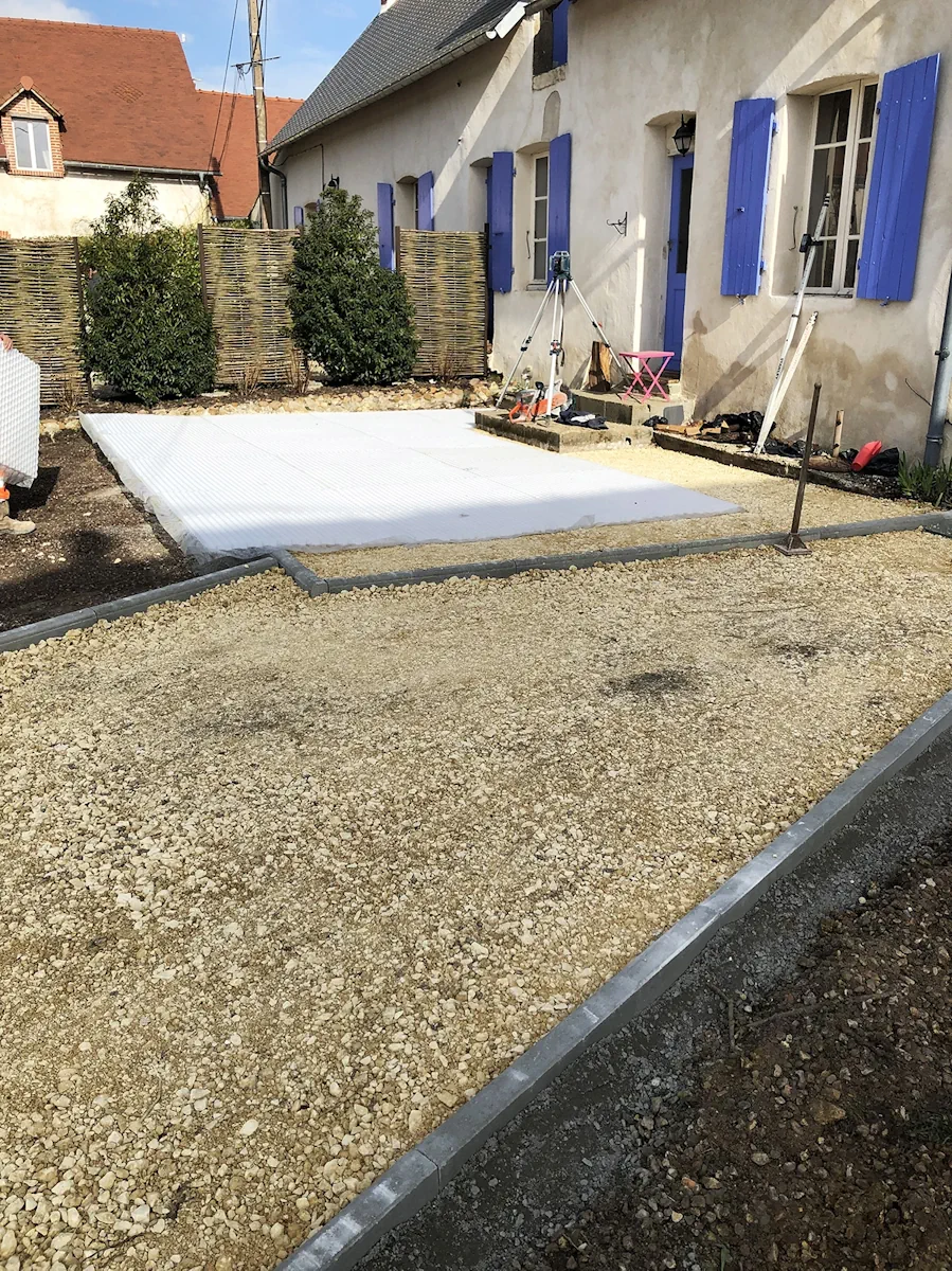 Cour en préparation devant une maison aux volets bleus, géotextile déroulé et bordures posées