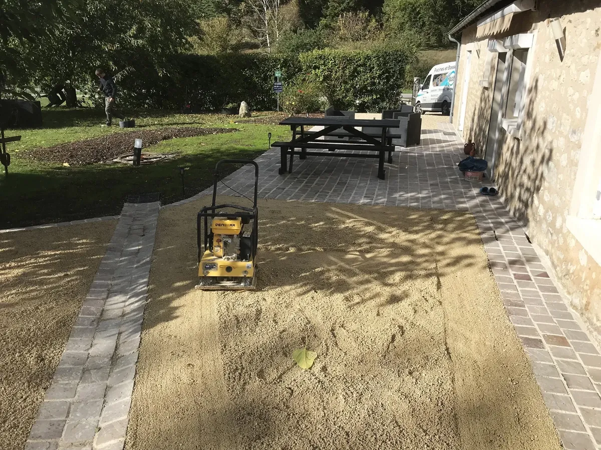Cour associant une terrasse pavée et une aire en gravier, séparées par une bande de pavés