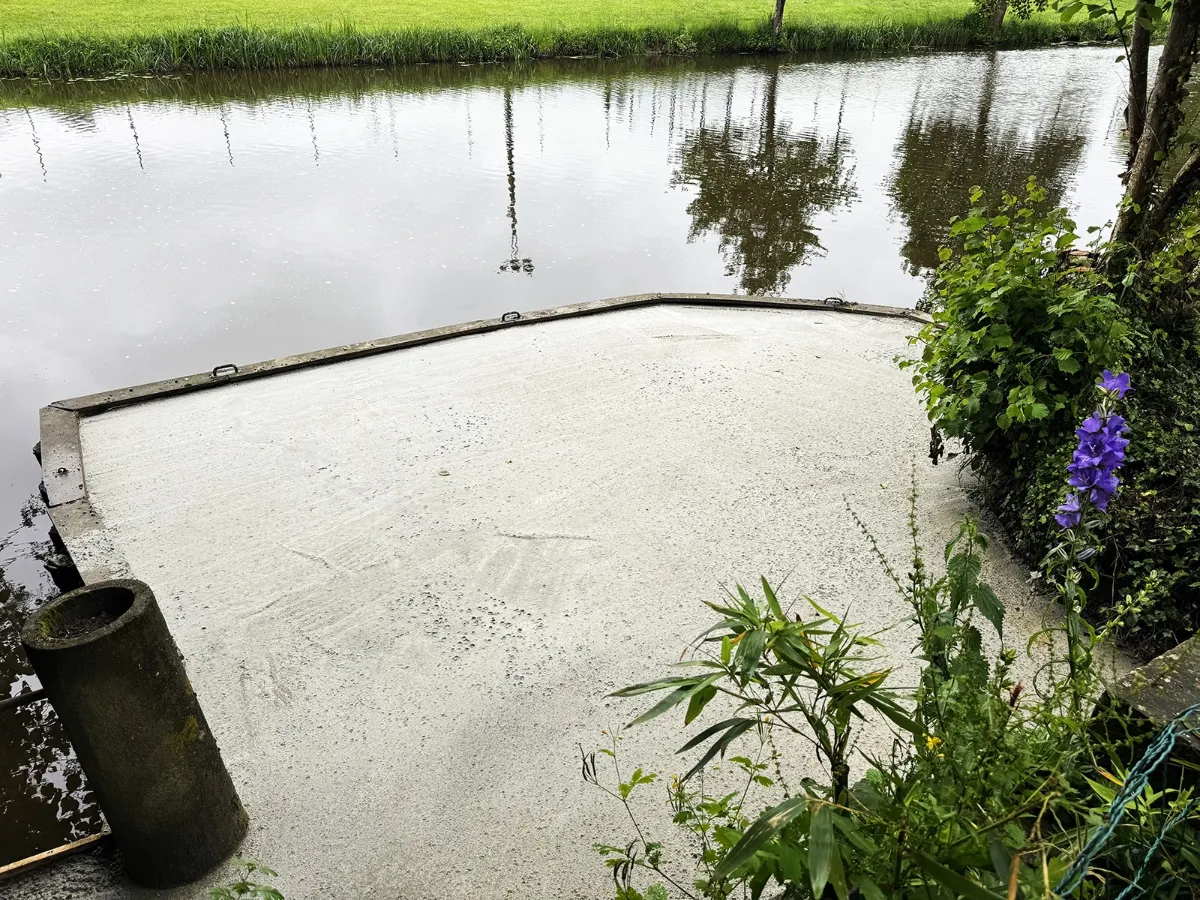 Cale en béton coulée au bord d'une rivière, bordée d'une murette et de végétation