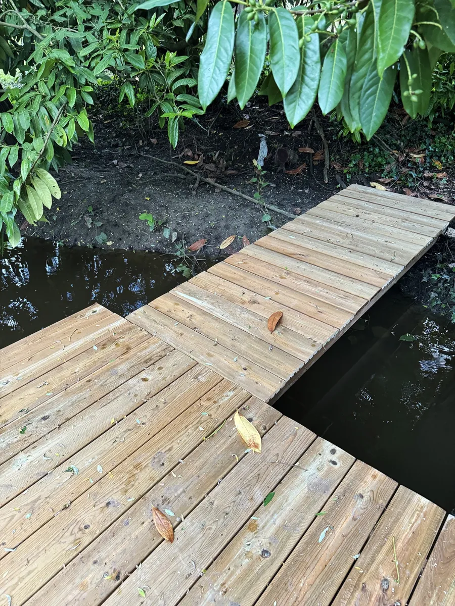Passerelle étroite en bois reliant la rive à un ponton plus large, au-dessus de l'eau
