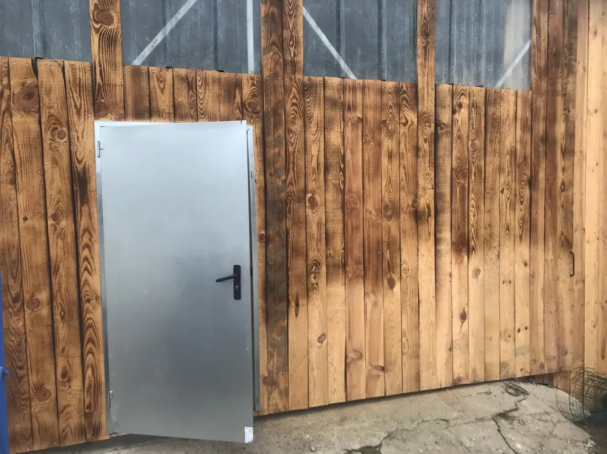 Détail d'un bardage en lames de bois brûlées au chalumeau, autour d'une porte de service métallique