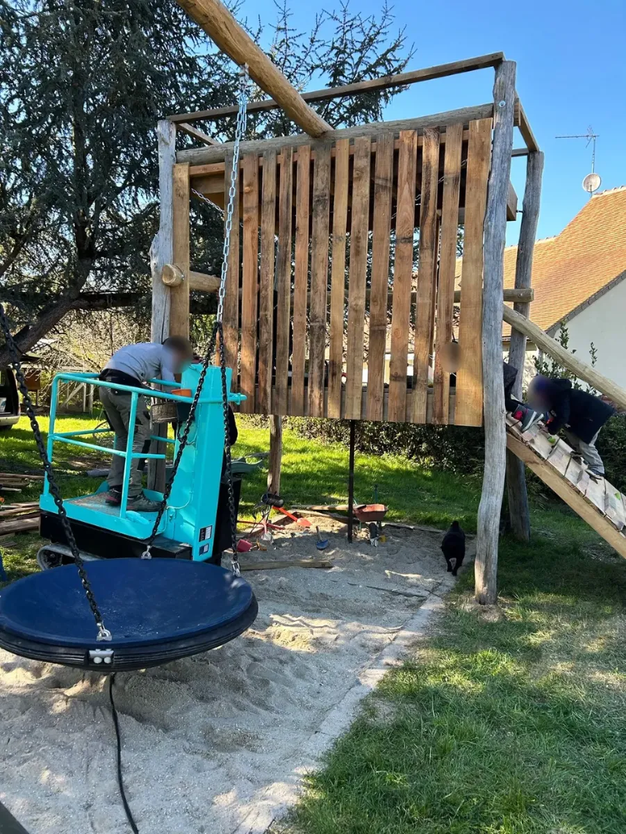 Cabane de jeux sur pilotis en cours de construction, balançoire nid et bac à sable déjà en place