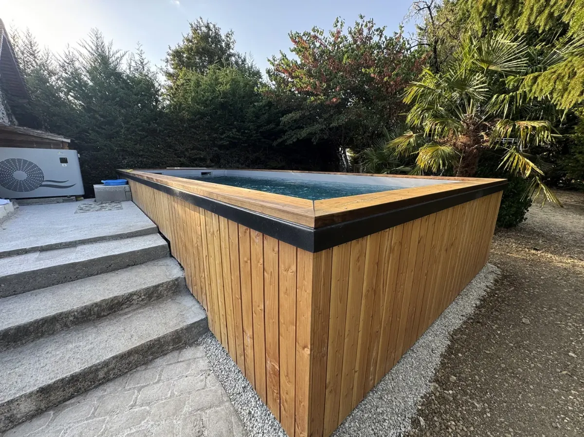 Piscine hors-sol habillée de lames de bois et coiffée d'une margelle noire, dans un jardin de campagne