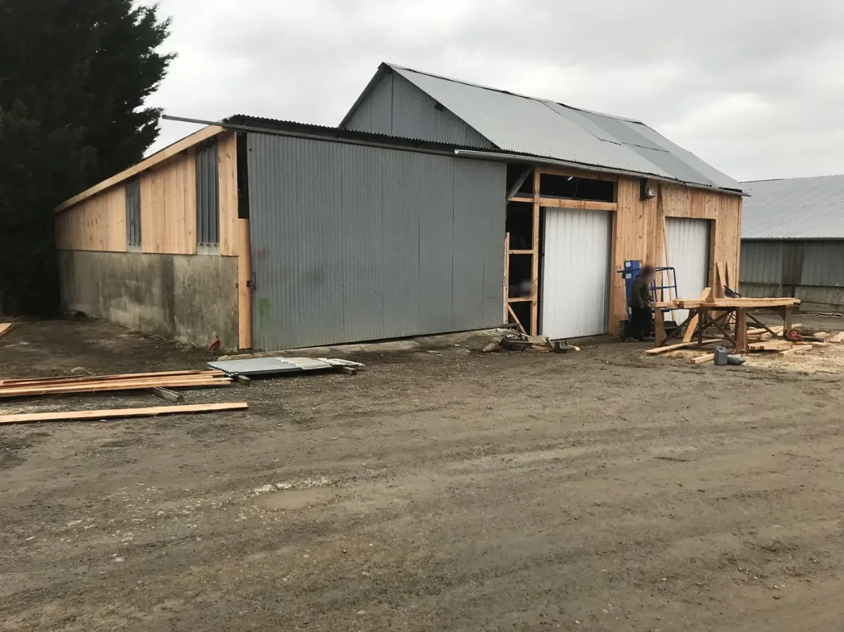 Hangar agricole en tôle avant travaux, premières lames de bardage bois posées sur le pignon