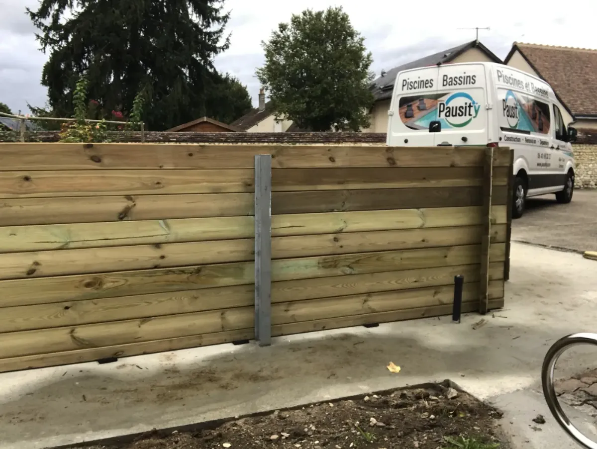 Mur de soutènement en madriers de bois horizontaux glissés entre des poteaux d'acier, fourgon Pausity à l'arrière