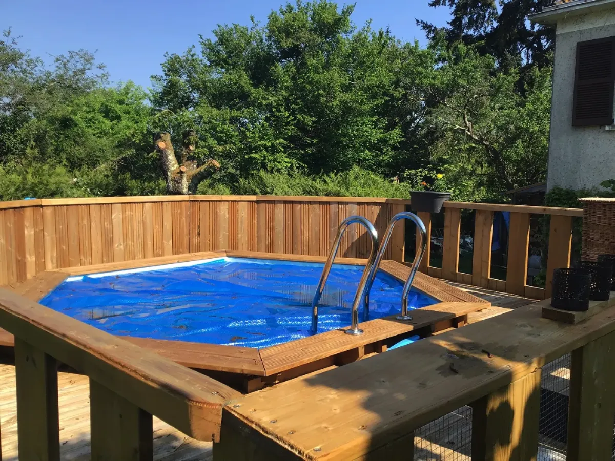 Échelle de piscine posée sur une terrasse en bois, palissade et massifs à l'arrière-plan