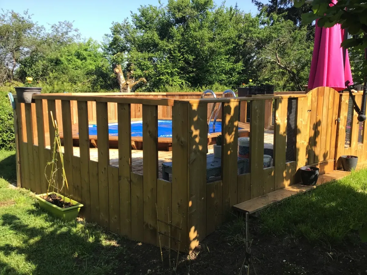 Terrasse en bois surélevée courant autour d'une piscine hors-sol, fermée par une balustrade à lames