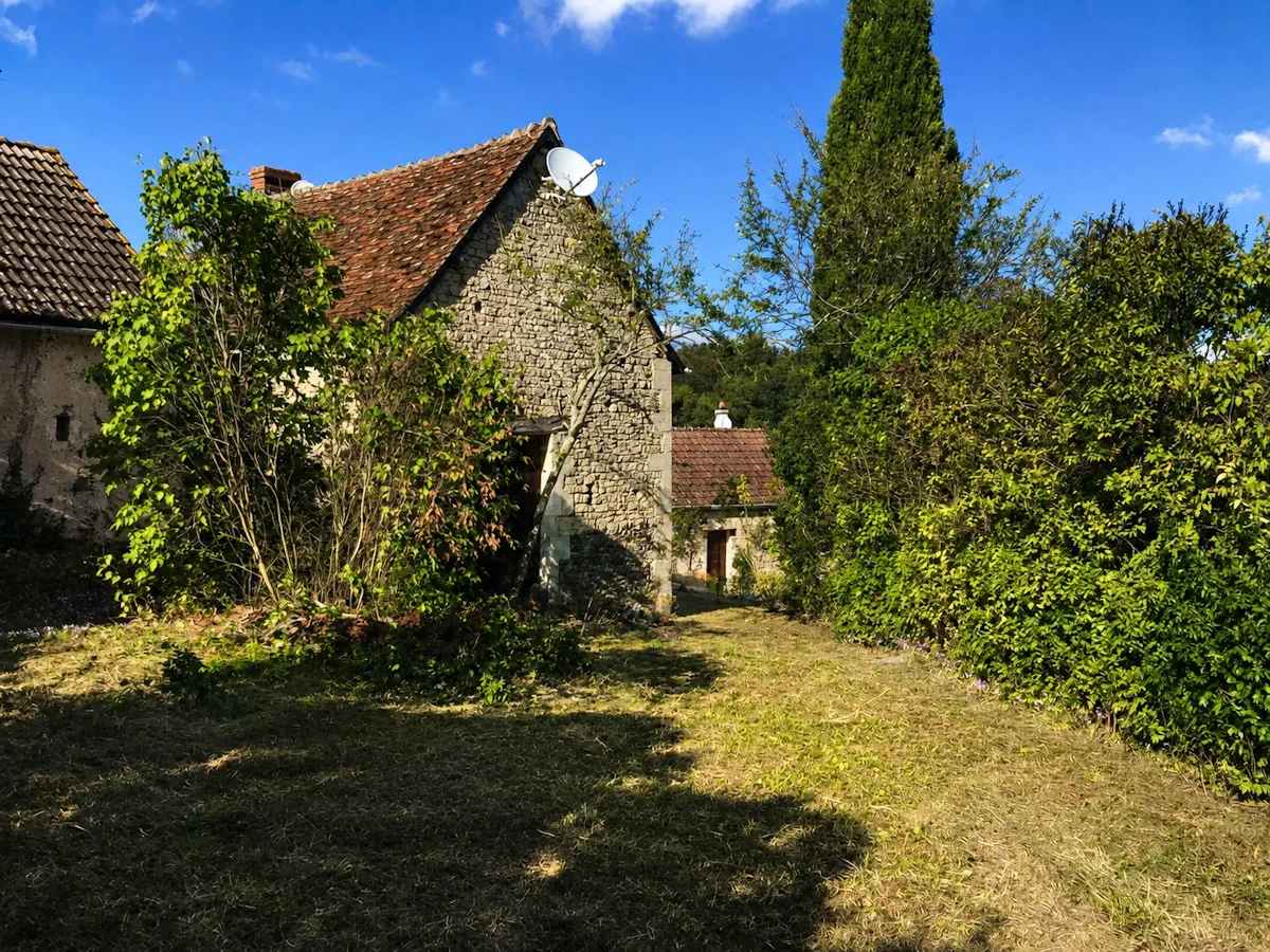 Cour d'une ferme ancienne fauchée entre les bâtiments de pierre, sous un ciel d'automne