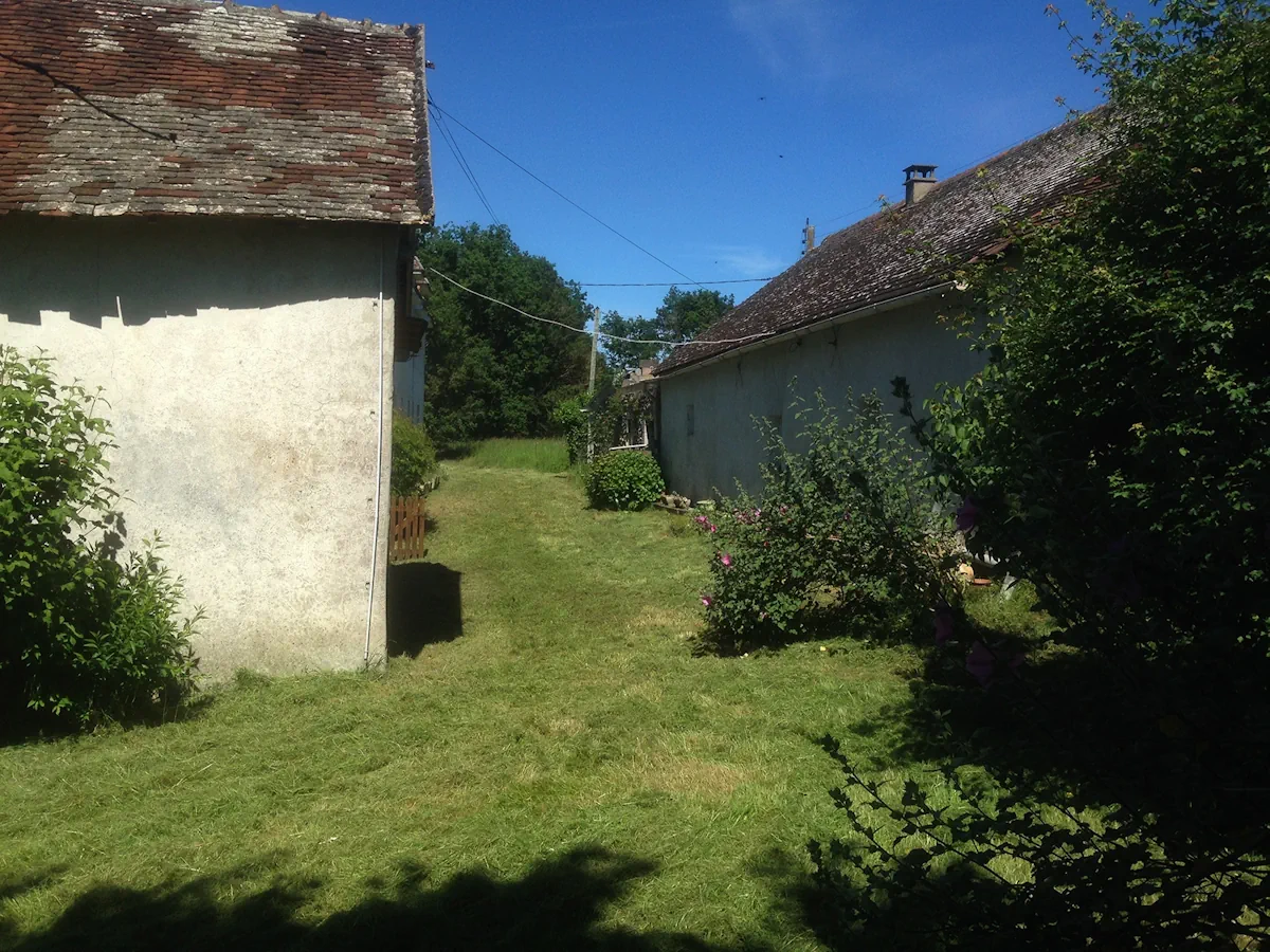 Passage entre deux bâtiments de ferme entièrement fauché, herbe coupée au sol, en plein été