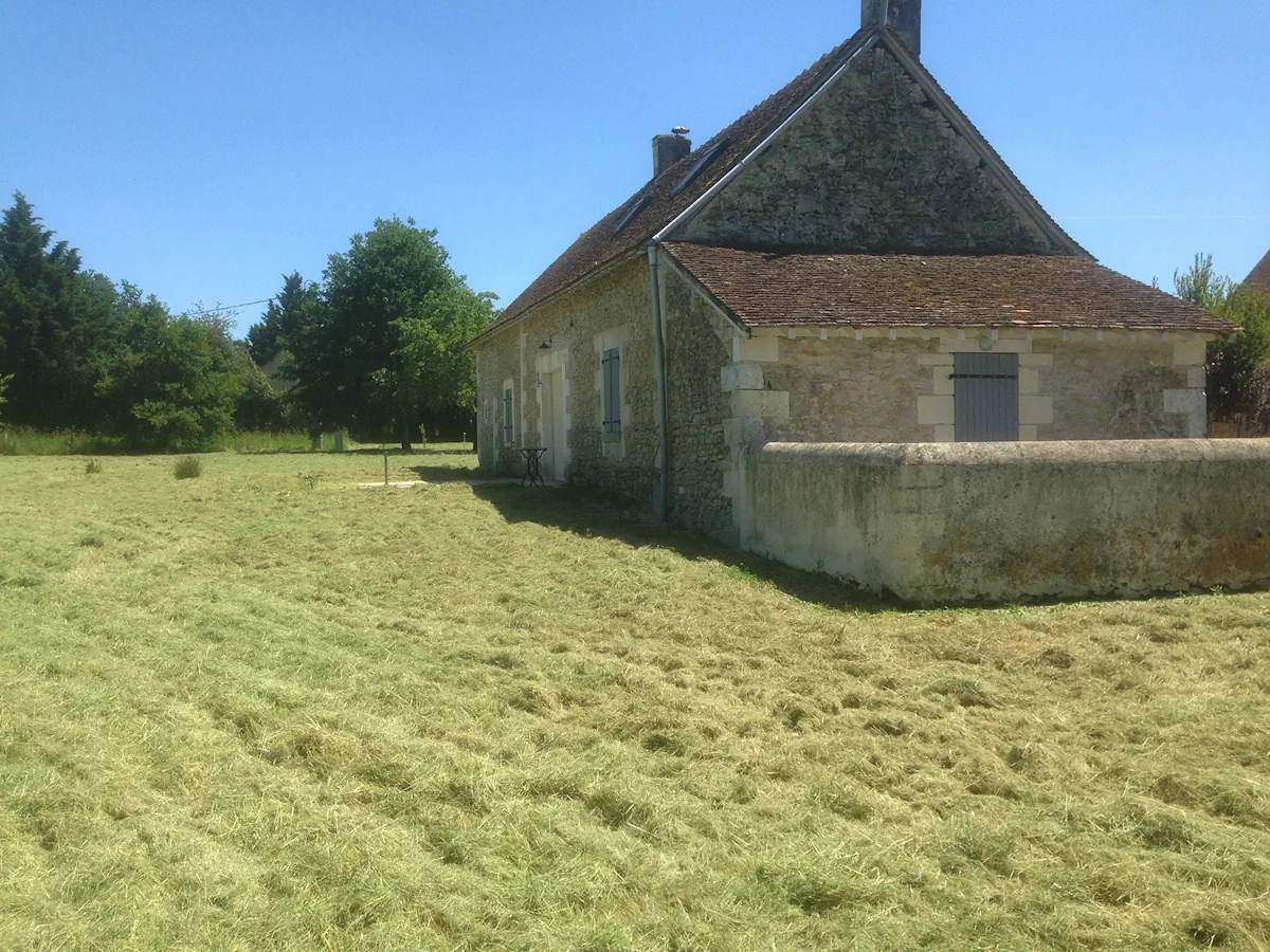Pignon d'une longère de pierre et son muret, au bord d'une prairie fraîchement fauchée
