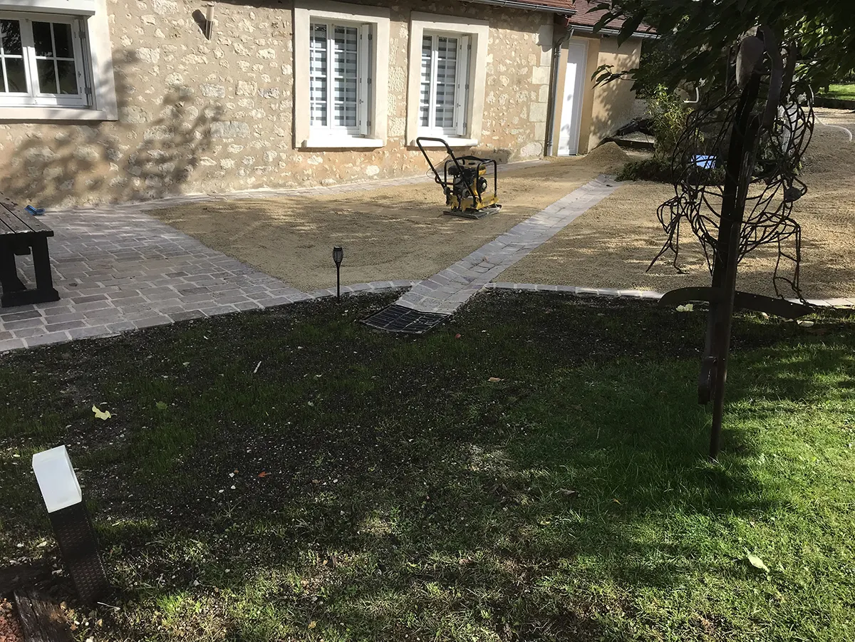 Aire de sable compactée à la plaque vibrante devant une maison de pierre