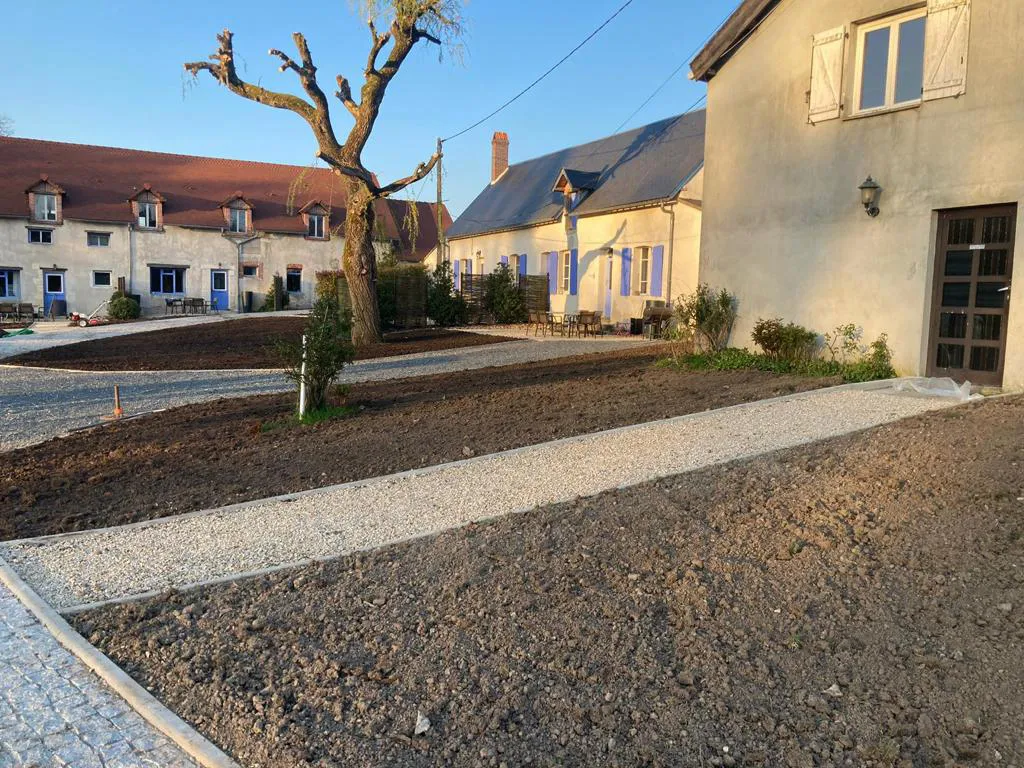 Cour de terre préparée et bande de gravier, au pied d'un saule têtard, entre les bâtiments