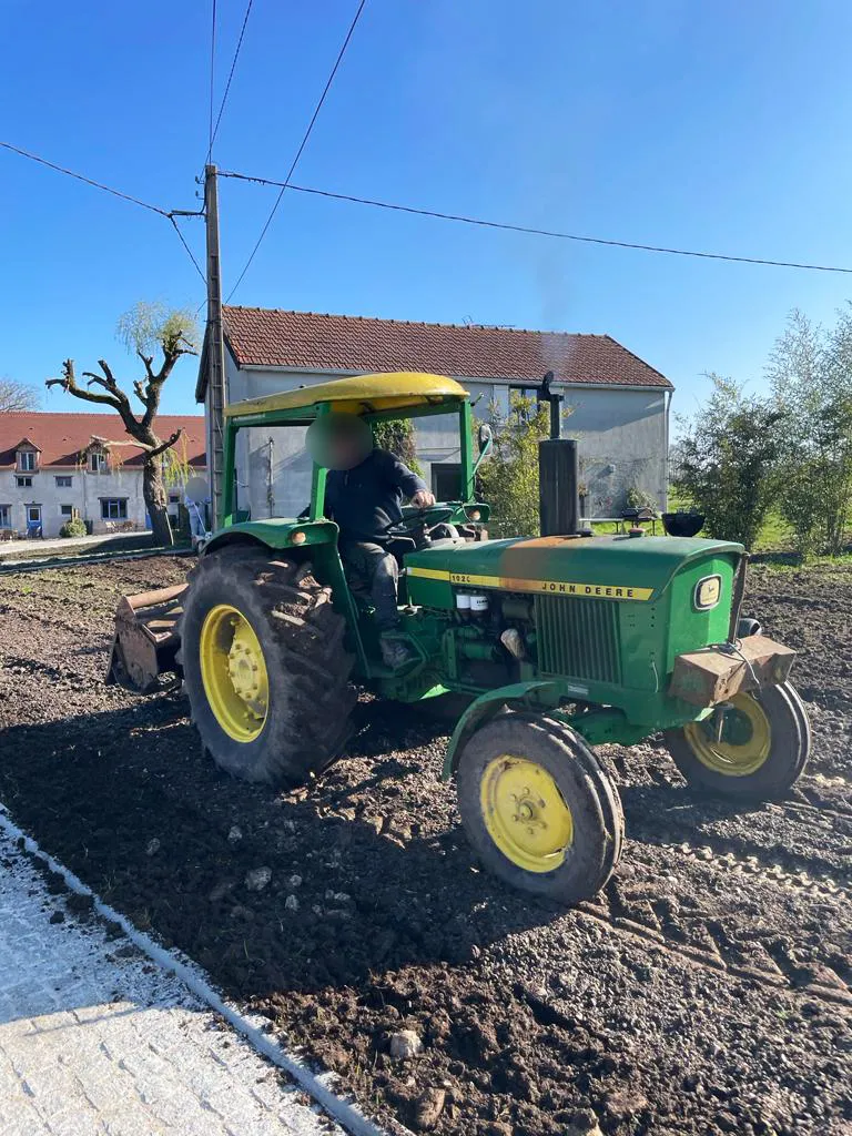 Tracteur agricole tirant une herse sur un terrain préparé avant engazonnement, en bordure de cour