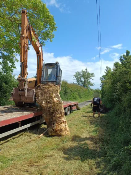 Bloc calcaire dressé sur un porte-engins, manœuvré à la pelle mécanique le long d'un chemin