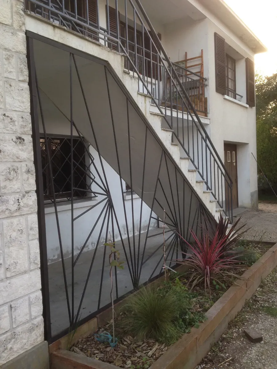 Garde-corps d'escalier extérieur et grille d'acier à motif rayonnant, sous une volée de marches