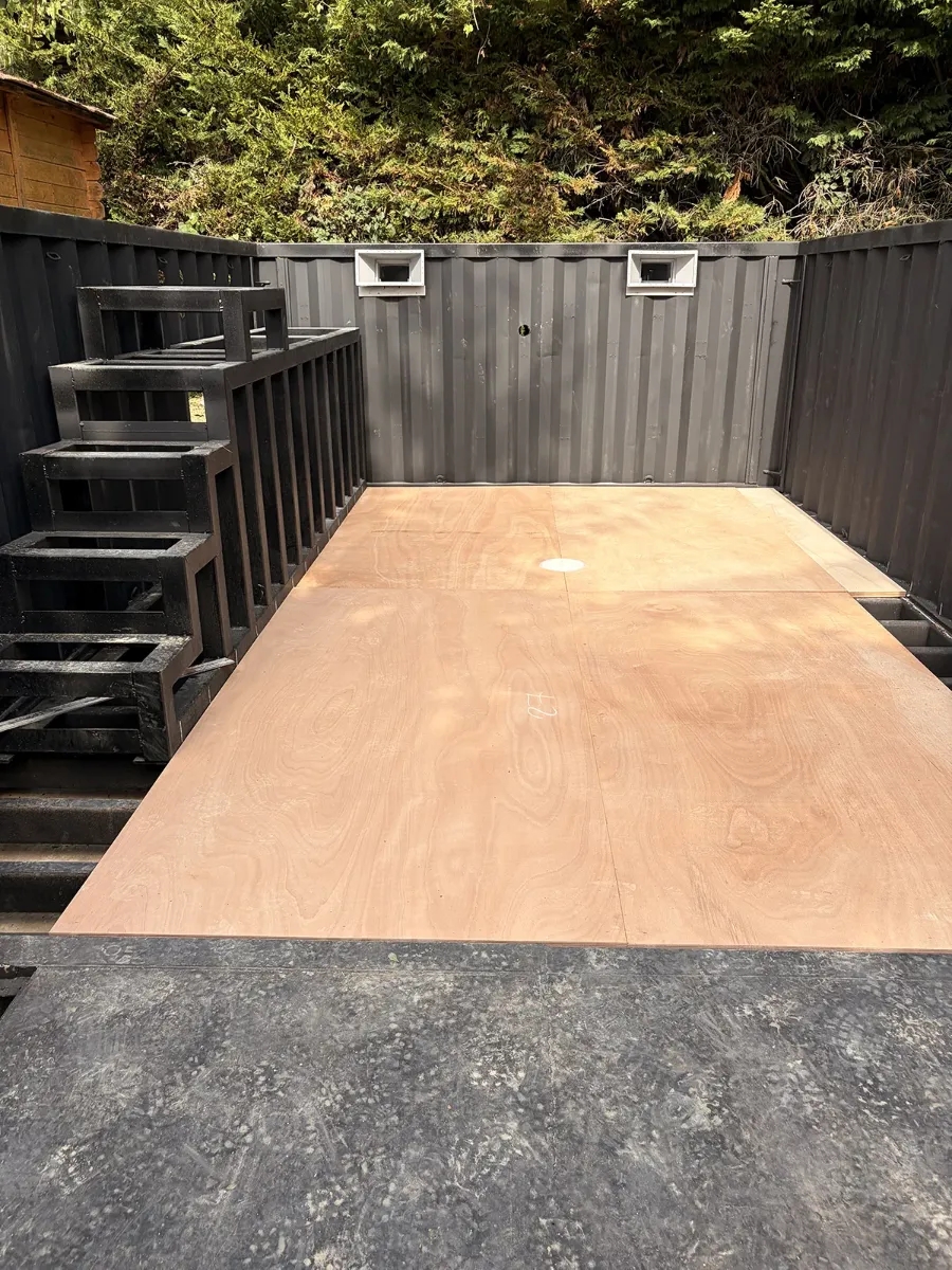 Plateforme d'acier noir recevant son plancher de bois, entre les parois d'un conteneur