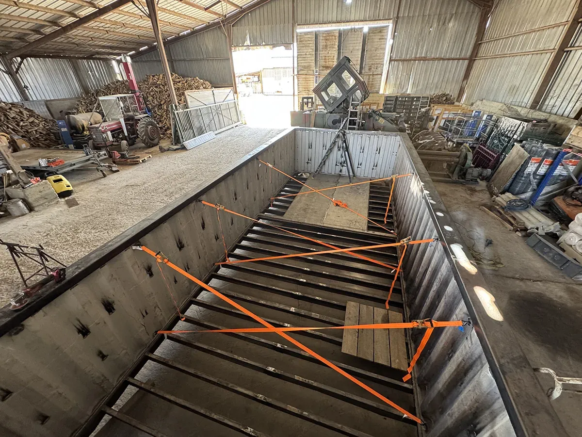 Longue structure d'acier sanglée sur son berceau dans un hangar, avant transport sur le chantier