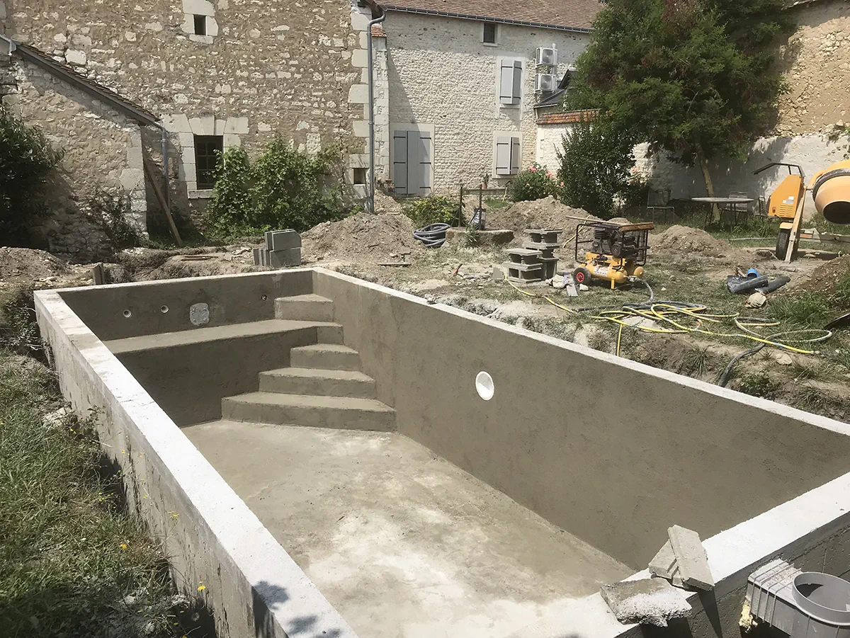 Bassin de piscine en béton avec son escalier maçonné, bétonnière et matériel de chantier autour