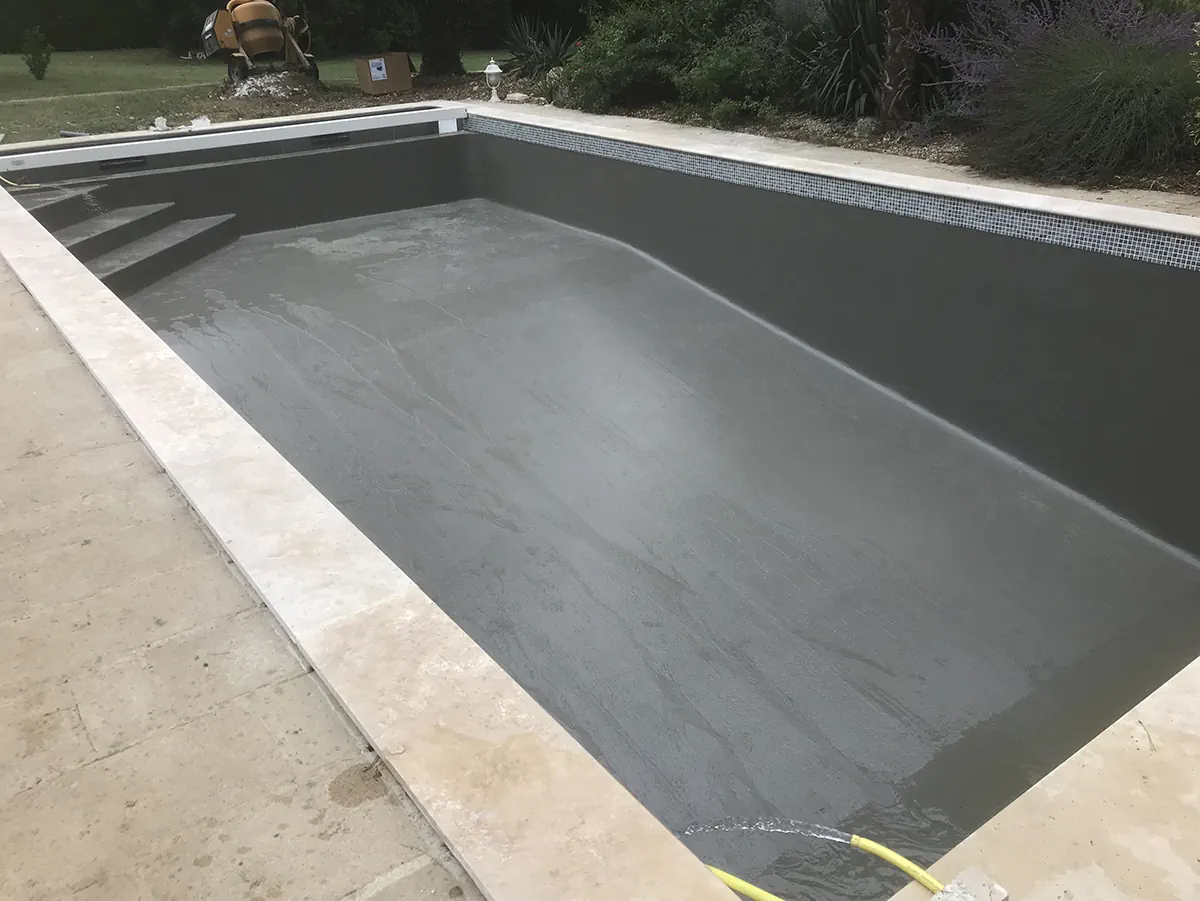 Bassin de piscine enduit de gris, margelles de travertin posées, bétonnière encore sur place