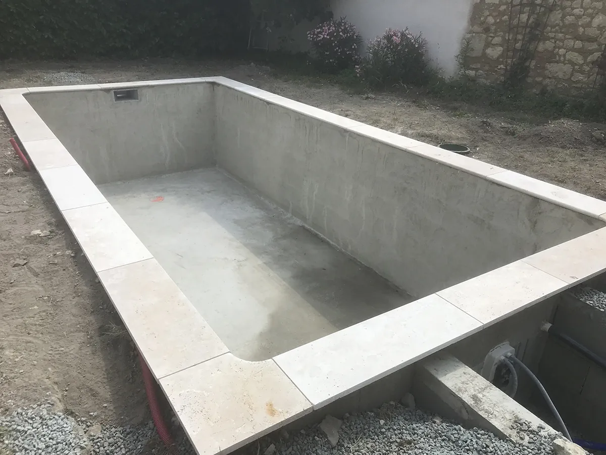 Bassin de piscine en béton lissé, ceinturé de margelles en pierre de taille, avant mise en eau