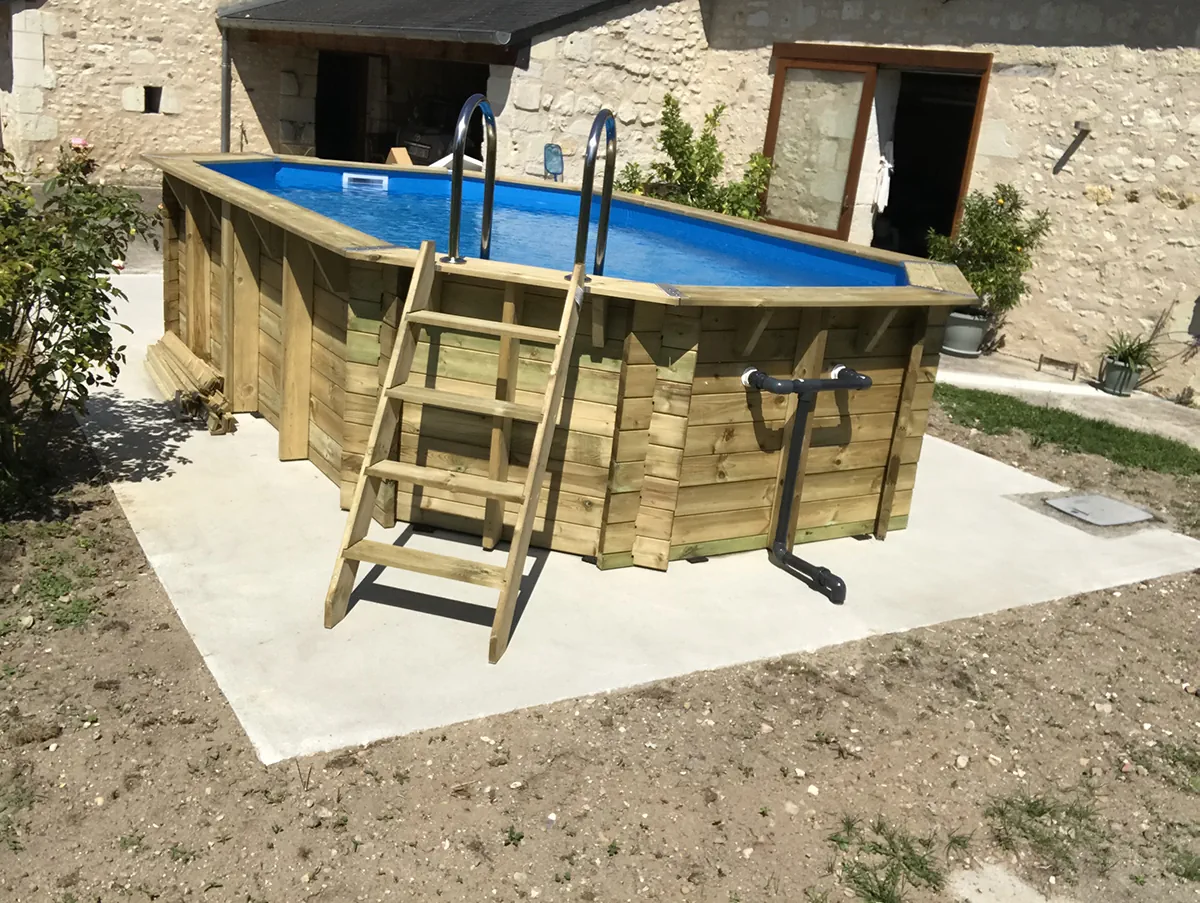 Piscine bois octogonale posée sur dalle béton avec son échelle, dans une cour de ferme en pierre