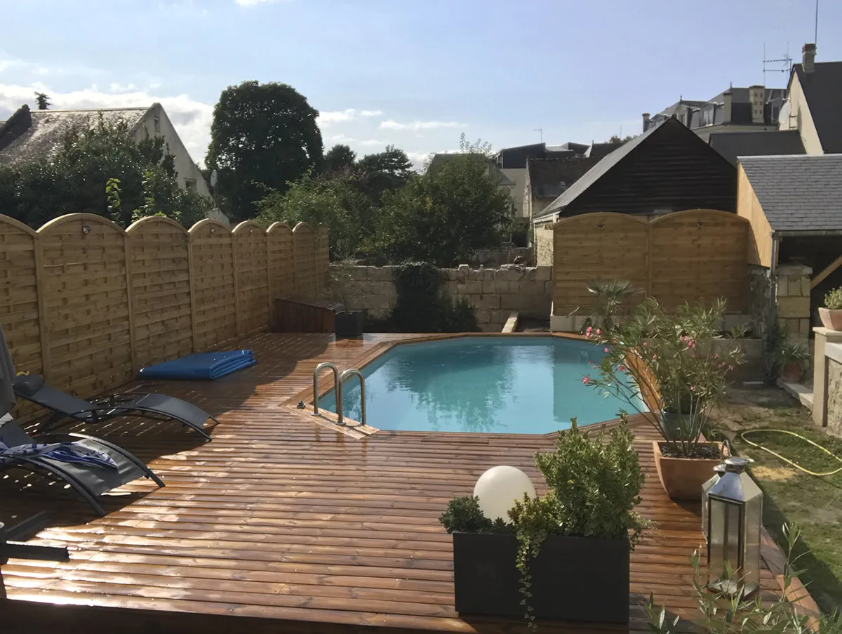 Piscine bois et sa terrasse meublée de transats et de lanternes, dans un jardin de ville