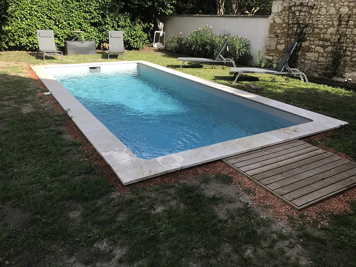 Piscine à margelle claire prolongée d'un caillebotis en bois, dans un jardin clos de murs