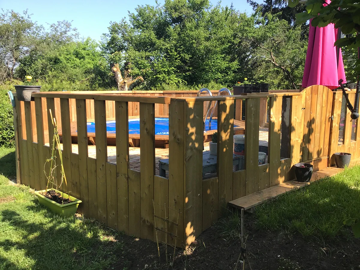Piscine hors-sol entourée d'une palissade de bois faisant barrière de sécurité, au fond d'un jardin