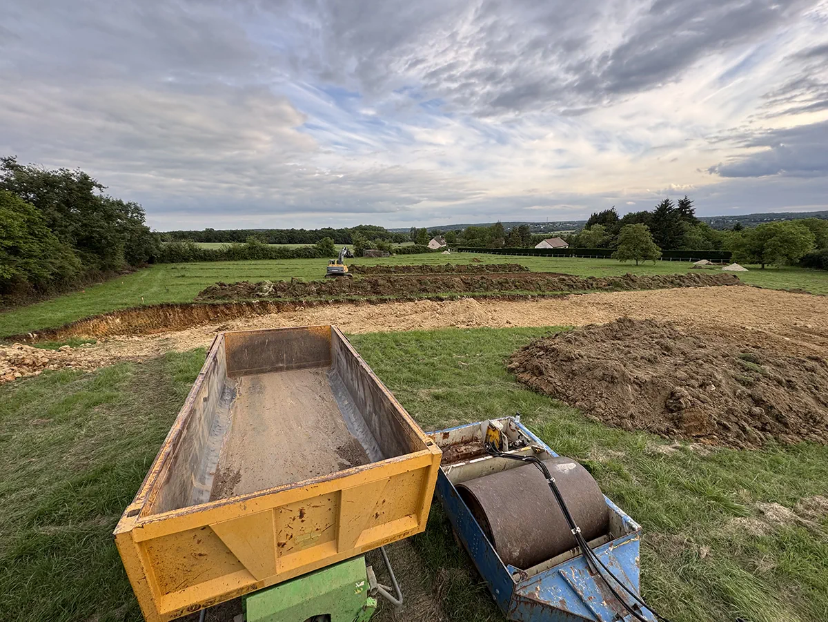 Benne et rouleau compacteur dételés au bord d'une plateforme terrassée, ouverte sur la campagne