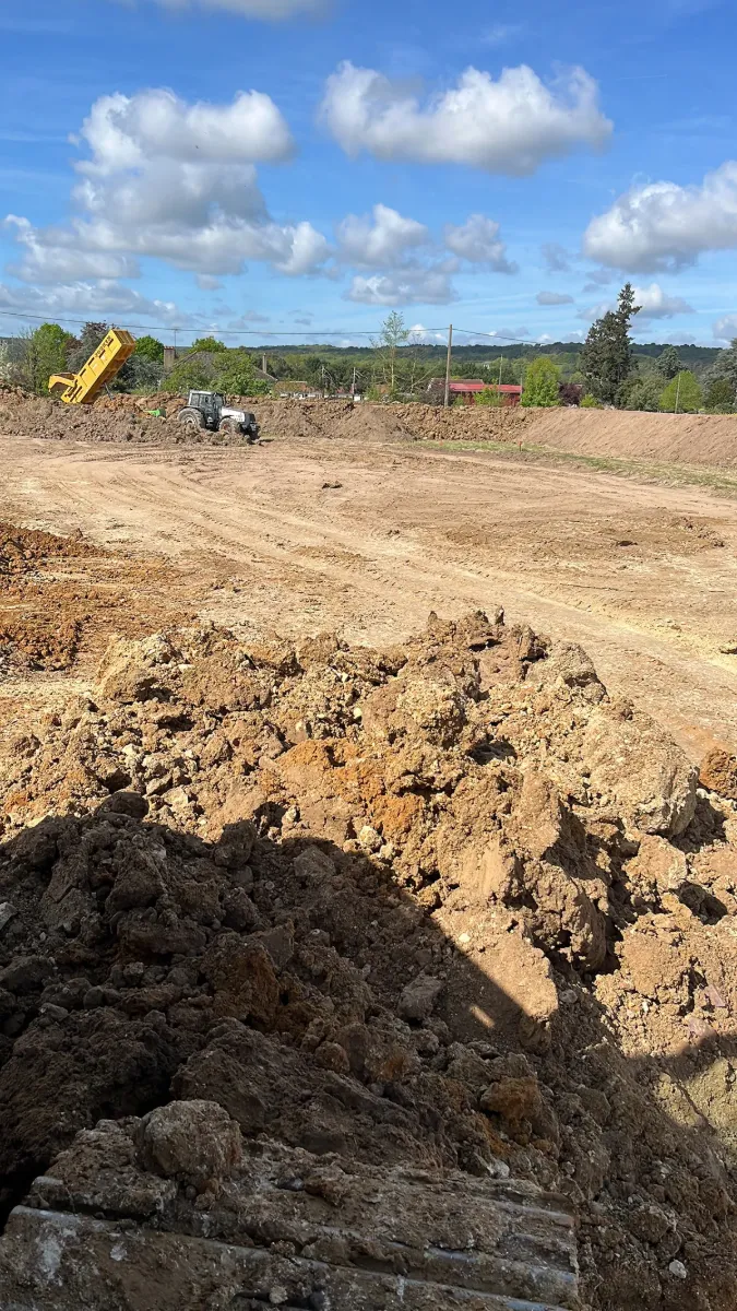 Vue large d'une plateforme terrassée, tracteur et benne au fond, merlons de terre sur les côtés