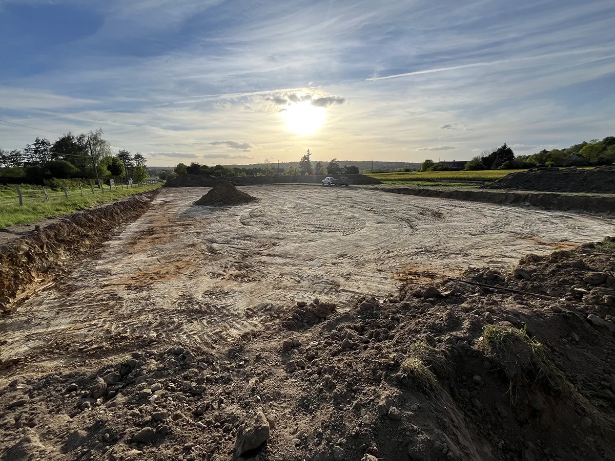 Grande plateforme terrassée et nivelée en plein champ, talus et merlons de terre, dans la lumière du soleil couchant