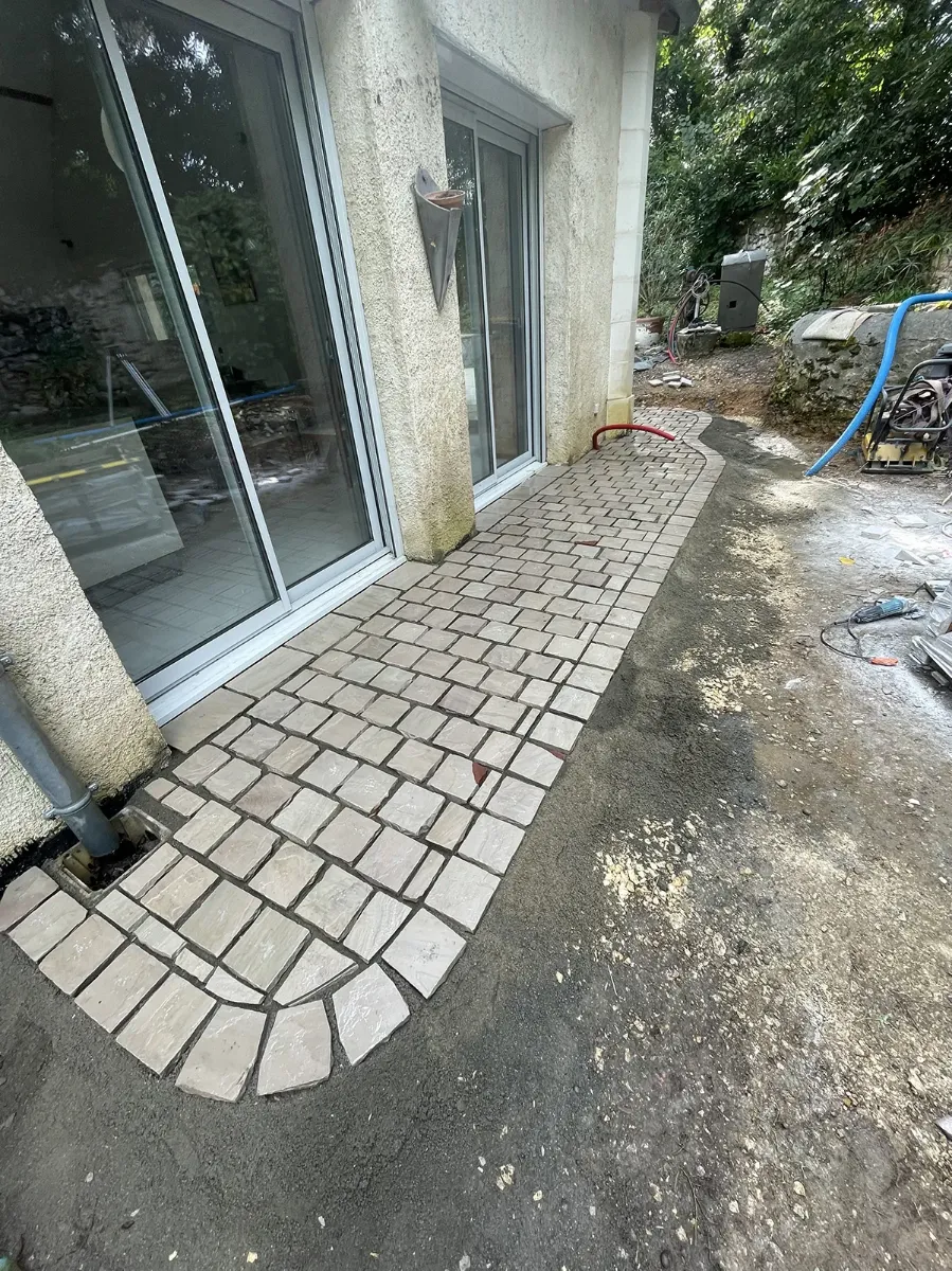 Cheminement en pavés de pierre longeant une maison et se terminant en arc de cercle