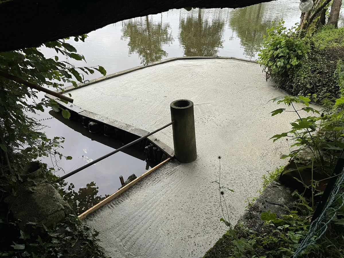 Plateforme de béton fraîchement coulée et talochée au bord d'une rivière, bitte d'amarrage en place