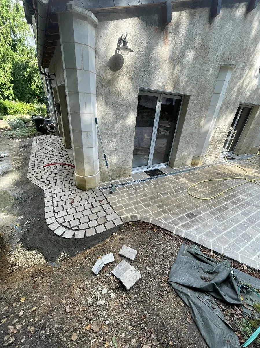 Raccord entre un cheminement en pavés et une terrasse en dalles de pierre, au pied d'une maison