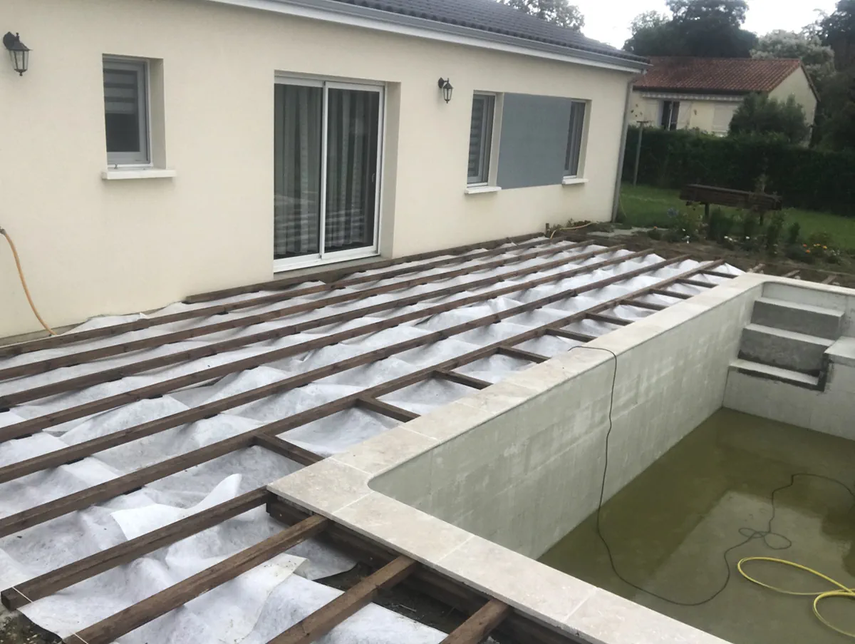 Solives de terrasse posées sur géotextile le long d'un bassin de piscine maçonné et margé