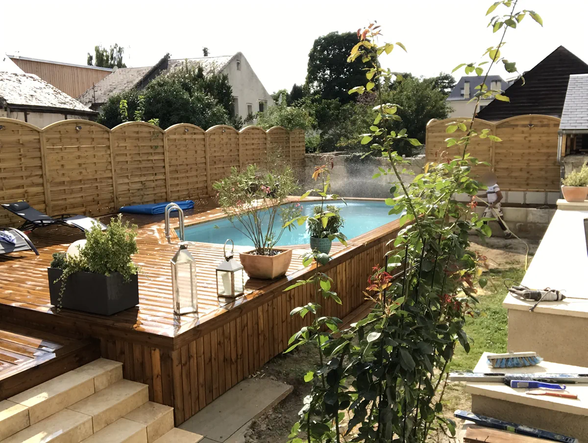 Terrasse en bois autour d'une piscine, garnie de jardinières et de lanternes, dans un jardin de ville