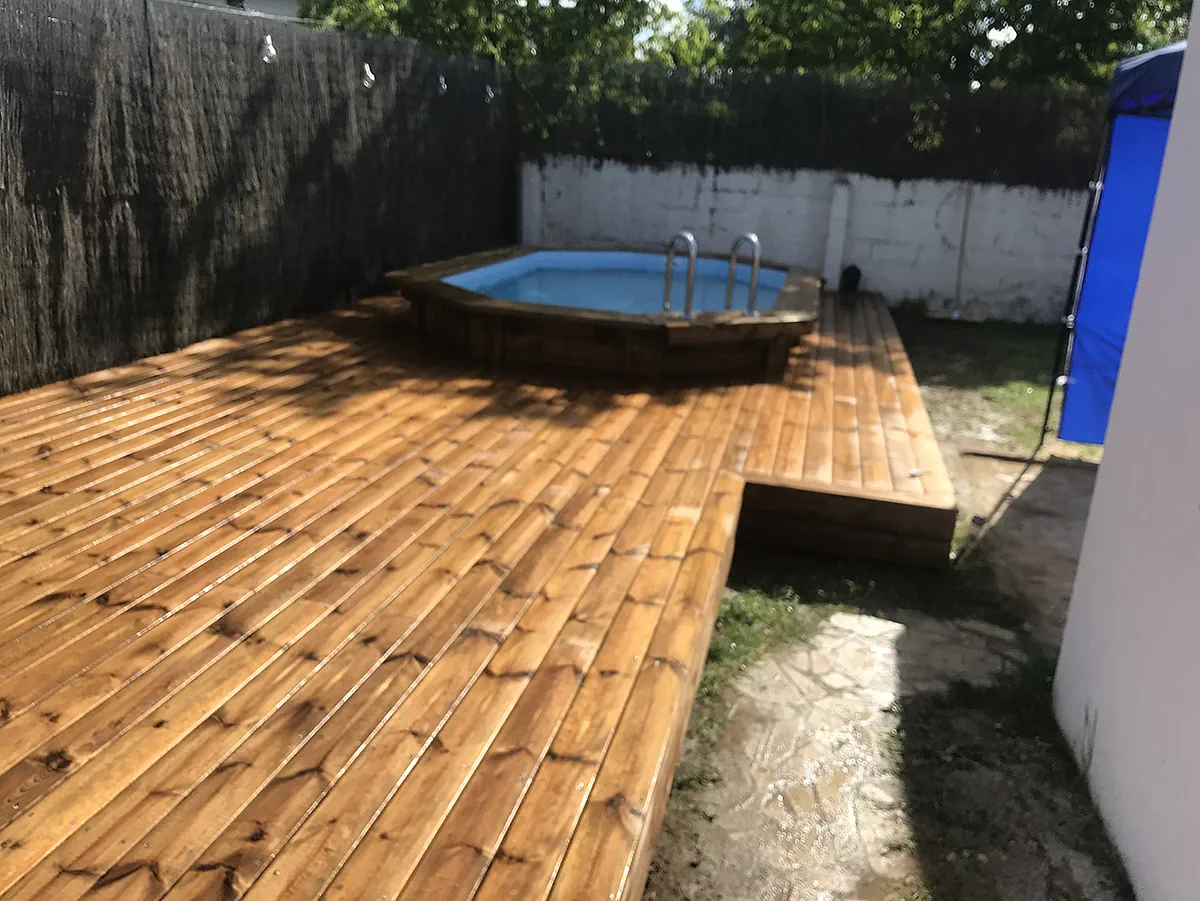 Large terrasse en lames de bois entourant une piscine octogonale, dans une cour close de murs