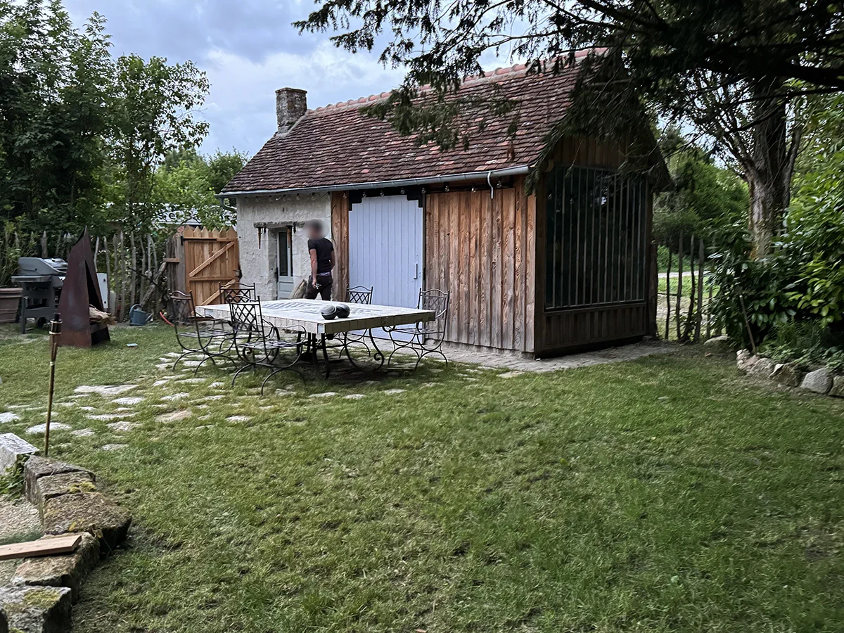 Terrasse carrelée et mobilier de jardin en fer forgé devant une grange de pierre restaurée