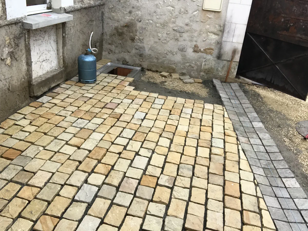 Terrasse en pavés de pierre dorée posée dans une cour fermée, bordure de pavés gris sur le côté