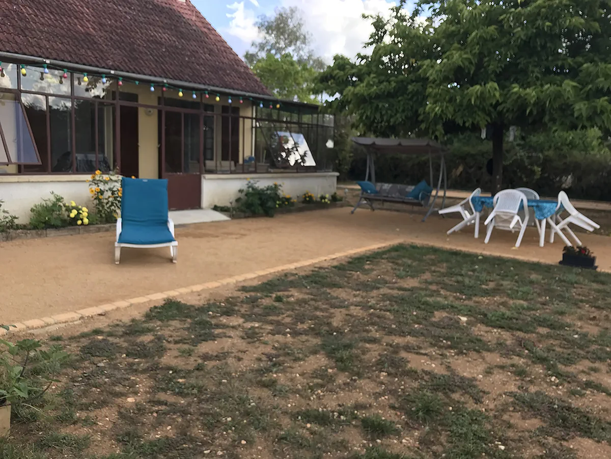 Terrasse de sable stabilisé aménagée devant une véranda, transat, balancelle et table de jardin